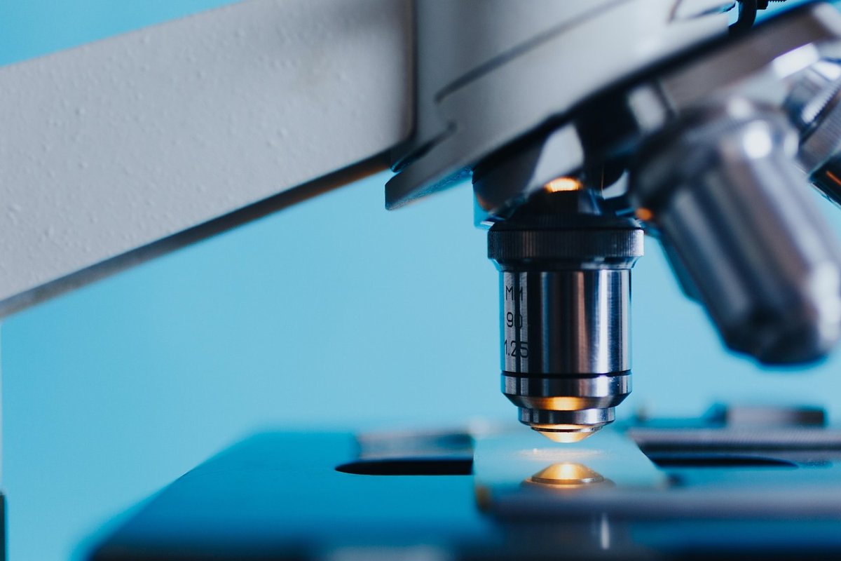 Close view of a laboratory microscope objective lens above a specimen stage under blue light