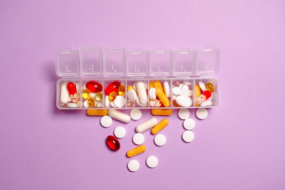 Open seven-day pill organizer filled with mixed capsules and tablets on a lavender surface